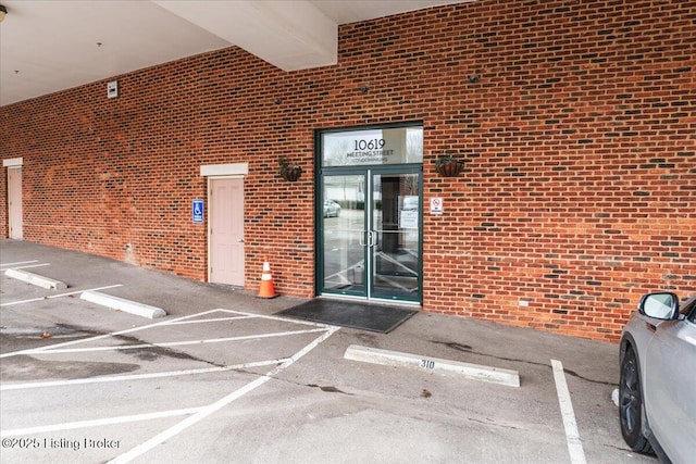 view of exterior entry with uncovered parking and brick siding