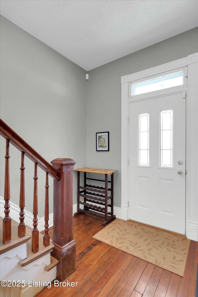 foyer entrance with a textured ceiling, baseboards, and hardwood / wood-style floors