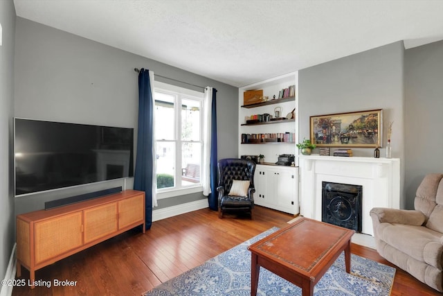 living room with built in shelves, a textured ceiling, wood-type flooring, a fireplace, and baseboards