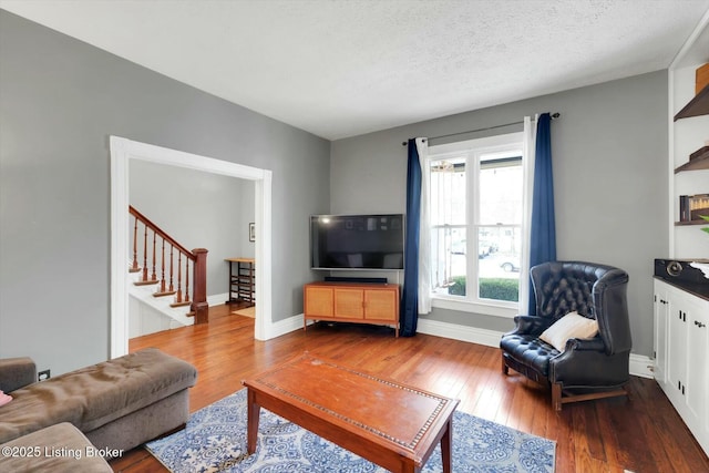 living area featuring stairway, a textured ceiling, baseboards, and wood-type flooring