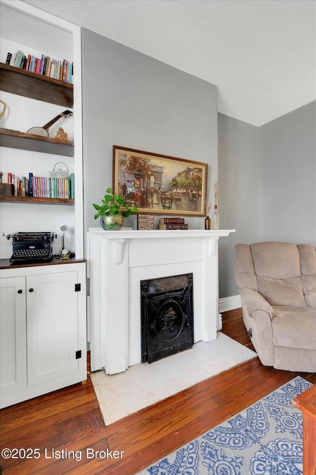 living area featuring a fireplace with flush hearth, wood finished floors, and a textured ceiling