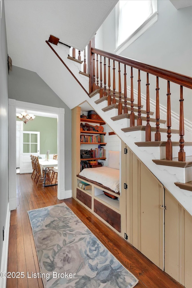 stairway featuring a wealth of natural light, a notable chandelier, hardwood / wood-style floors, and vaulted ceiling