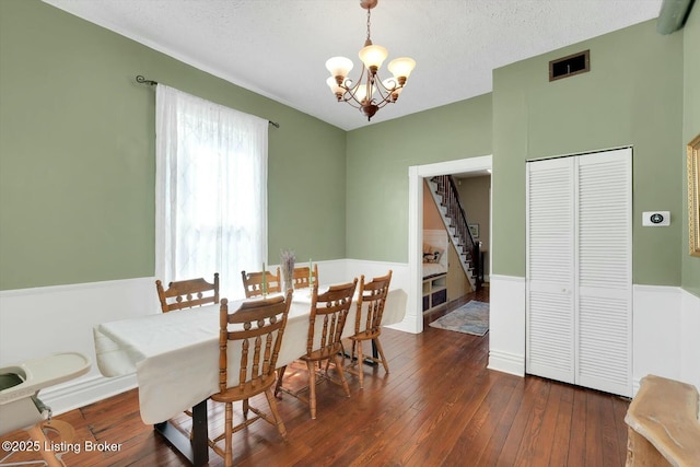 dining room featuring visible vents, dark wood-style flooring, a textured ceiling, a chandelier, and stairs