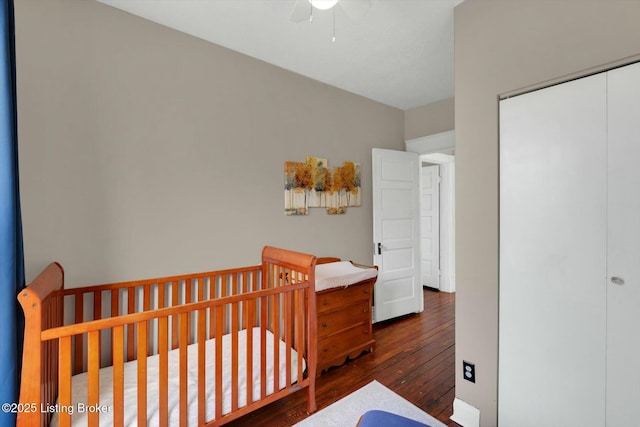 bedroom with a closet, a crib, dark wood-type flooring, and a ceiling fan