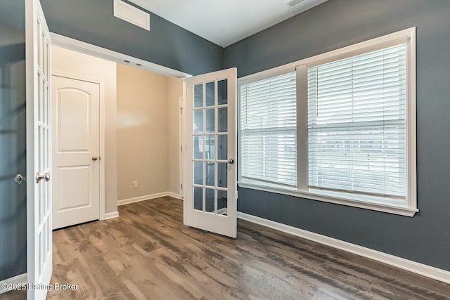 empty room with french doors, wood finished floors, visible vents, and baseboards