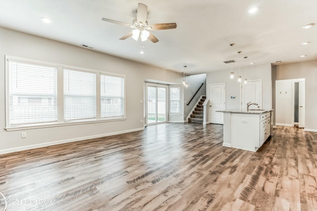 unfurnished living room with a sink, wood finished floors, visible vents, baseboards, and stairway