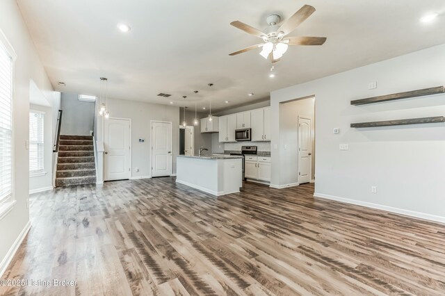 kitchen featuring open floor plan, stainless steel microwave, a sink, and white cabinetry