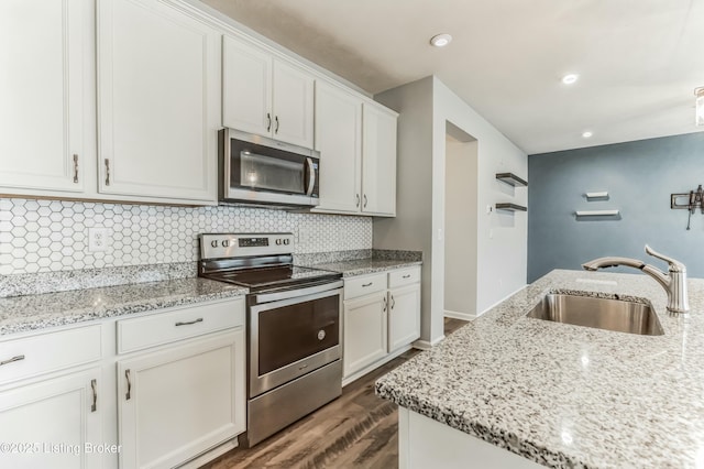 kitchen featuring white cabinets, dark wood finished floors, a sink, stainless steel appliances, and backsplash