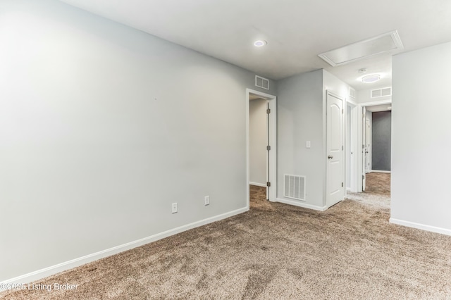 carpeted empty room with attic access, visible vents, and baseboards