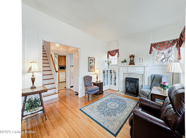 living room with a fireplace with flush hearth, ornamental molding, stairway, and light wood finished floors