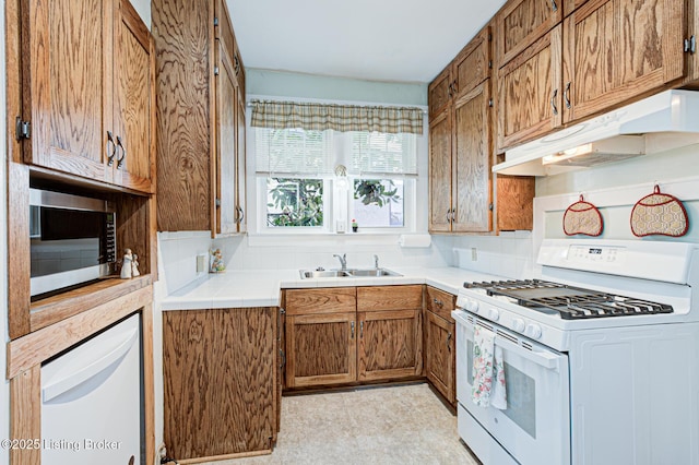 kitchen featuring white gas range, stainless steel microwave, brown cabinets, under cabinet range hood, and a sink