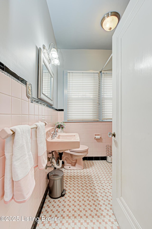 full bathroom featuring a wainscoted wall, tile patterned floors, toilet, a sink, and tile walls