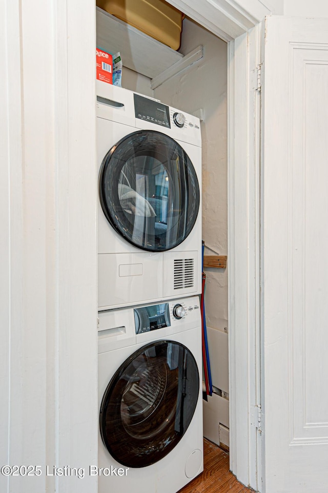 washroom with wood finished floors, stacked washer / drying machine, and laundry area