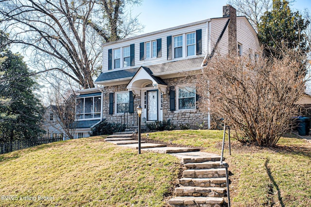 view of front facade with stone siding, fence, a chimney, a front yard, and roof with shingles