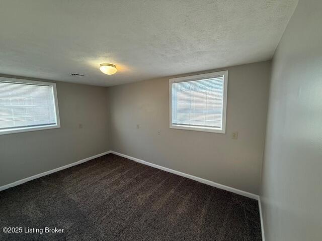 spare room featuring visible vents, baseboards, dark carpet, and a textured ceiling