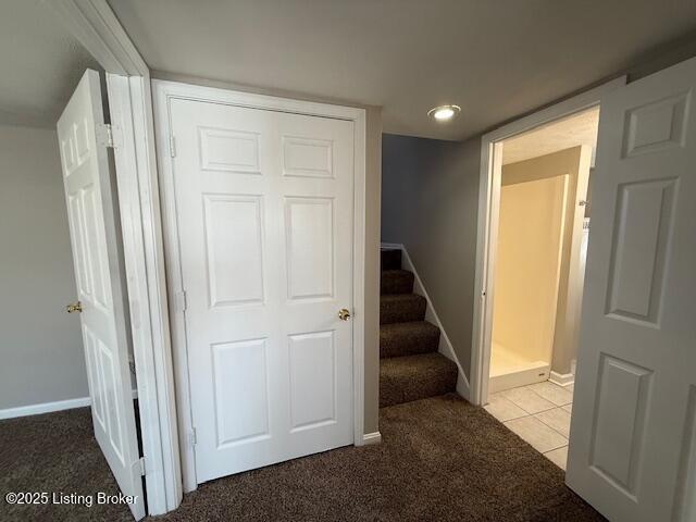 corridor with light tile patterned flooring, light colored carpet, baseboards, and stairs