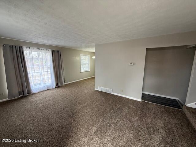 spare room featuring baseboards, visible vents, dark colored carpet, and a textured ceiling