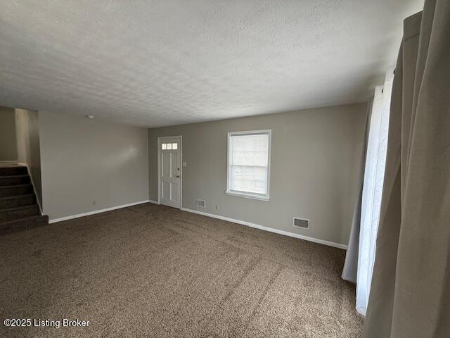 unfurnished room with visible vents, a textured ceiling, baseboards, and stairs