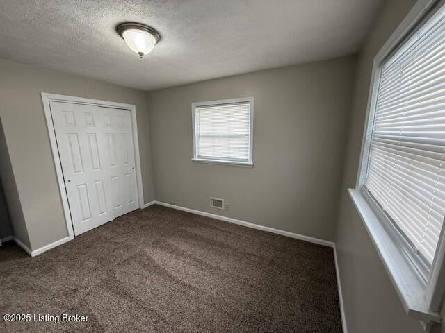 unfurnished bedroom with a textured ceiling, visible vents, baseboards, a closet, and dark colored carpet