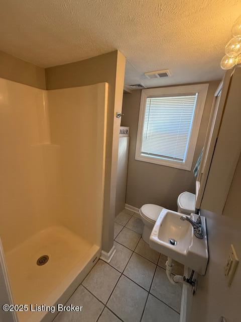 bathroom featuring a textured ceiling, tile patterned flooring, toilet, visible vents, and a stall shower