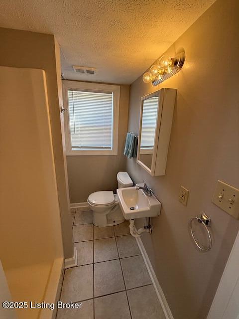 bathroom featuring a textured ceiling, tile patterned flooring, toilet, a sink, and visible vents