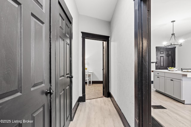 hall featuring light wood-style floors, baseboards, and a notable chandelier