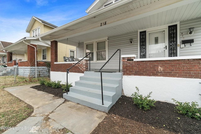 view of exterior entry featuring a porch, fence, and brick siding