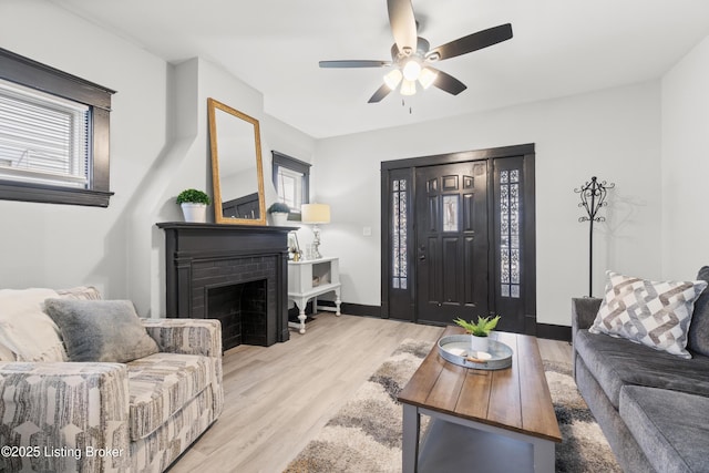 living area featuring a brick fireplace, a ceiling fan, baseboards, and wood finished floors