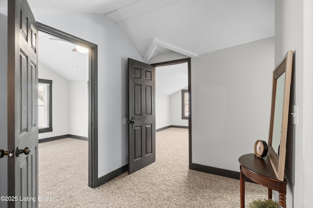 hall featuring baseboards, vaulted ceiling, and light colored carpet