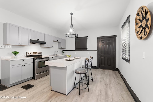 kitchen with under cabinet range hood, stainless steel electric range oven, a kitchen breakfast bar, and light wood-style flooring