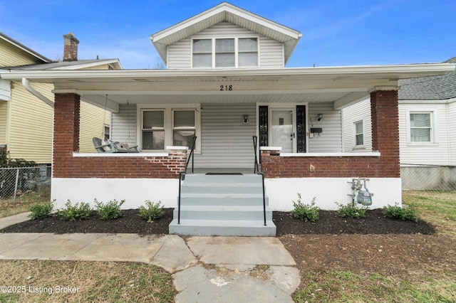 bungalow-style house with covered porch, brick siding, and fence