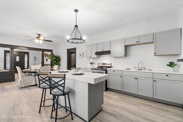 kitchen featuring under cabinet range hood, a sink, light countertops, stainless steel electric range, and gray cabinets