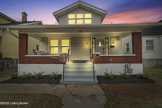 view of front facade featuring covered porch, brick siding, and fence