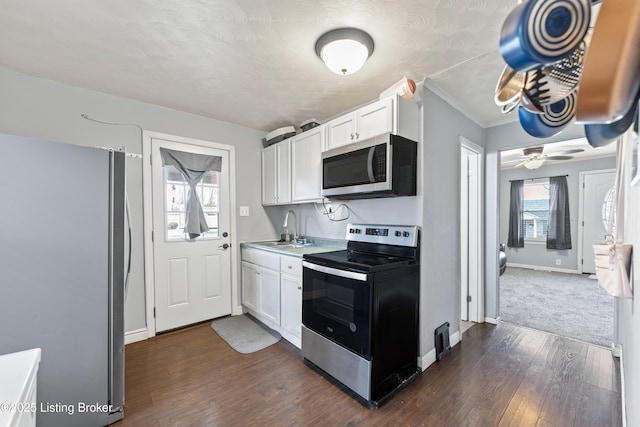 kitchen with stainless steel appliances, dark wood-type flooring, a sink, white cabinetry, and baseboards