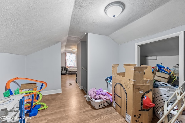 interior space with a textured ceiling, baseboards, vaulted ceiling, and wood finished floors