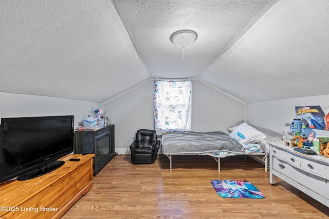 bedroom featuring a textured ceiling, vaulted ceiling, and wood finished floors