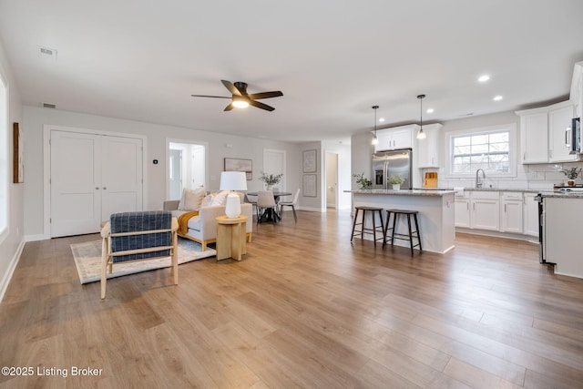 living room featuring ceiling fan, baseboards, light wood-style flooring, and recessed lighting