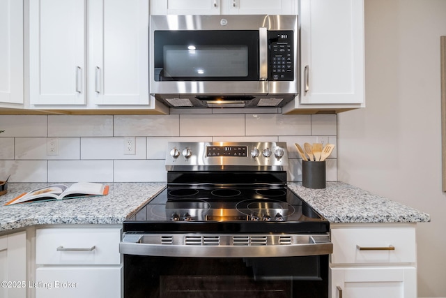 kitchen with stainless steel appliances, white cabinets, light stone counters, and tasteful backsplash