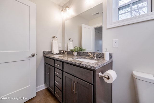 bathroom featuring toilet, double vanity, a sink, and visible vents