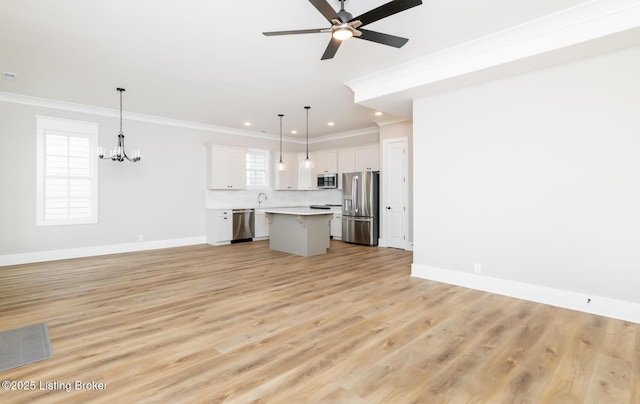 unfurnished living room with ceiling fan with notable chandelier, light wood-type flooring, a wealth of natural light, and crown molding