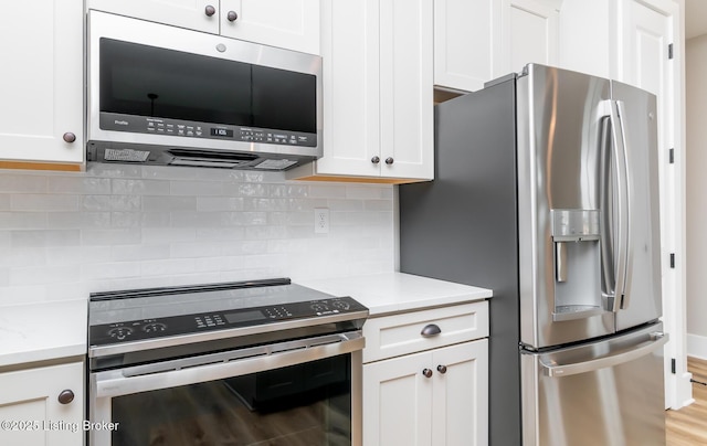 kitchen with appliances with stainless steel finishes, white cabinetry, light wood-style flooring, and backsplash