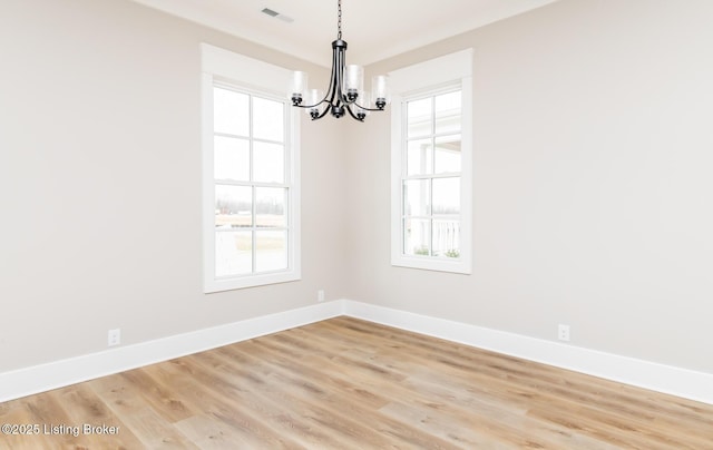 empty room featuring a chandelier, light wood-type flooring, visible vents, and baseboards