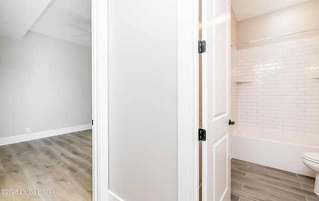 bathroom featuring  shower combination, wood finished floors, toilet, and baseboards