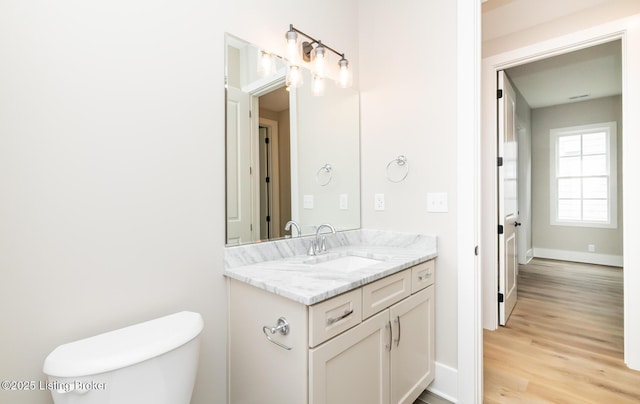 bathroom featuring toilet, baseboards, wood finished floors, and vanity