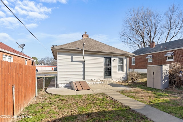 back of property with a patio, a shingled roof, a chimney, and fence