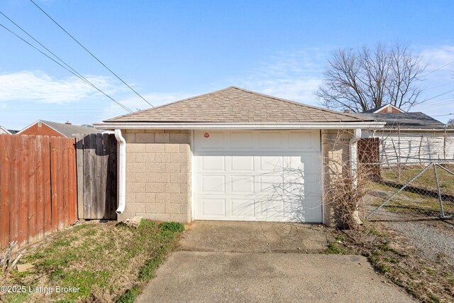 view of side of home featuring driveway, concrete block siding, roof with shingles, and fence