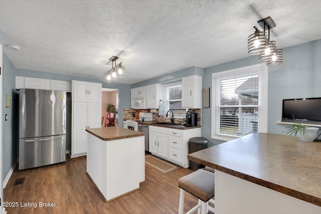 kitchen featuring dark wood-style flooring, a sink, stainless steel appliances, white cabinetry, and dark countertops