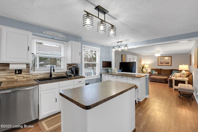 kitchen with dark countertops, a sink, a center island, and stainless steel dishwasher