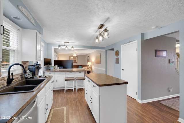 kitchen featuring a sink, stainless steel dishwasher, a peninsula, and wood finished floors