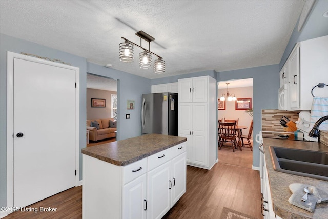 kitchen with dark countertops, freestanding refrigerator, dark wood-type flooring, and a sink